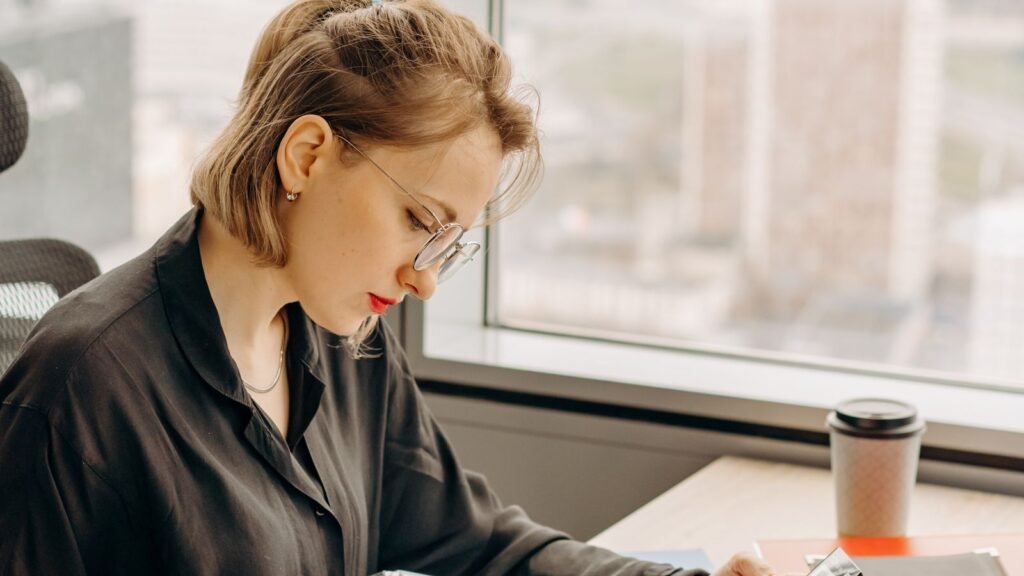 Une femme travaille sur des documents avec une calculatrice, près d’une fenêtre