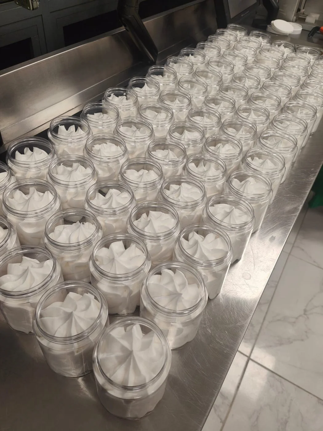 Pots de crème remplis alignés sur un plan de travail inox avant fermeture