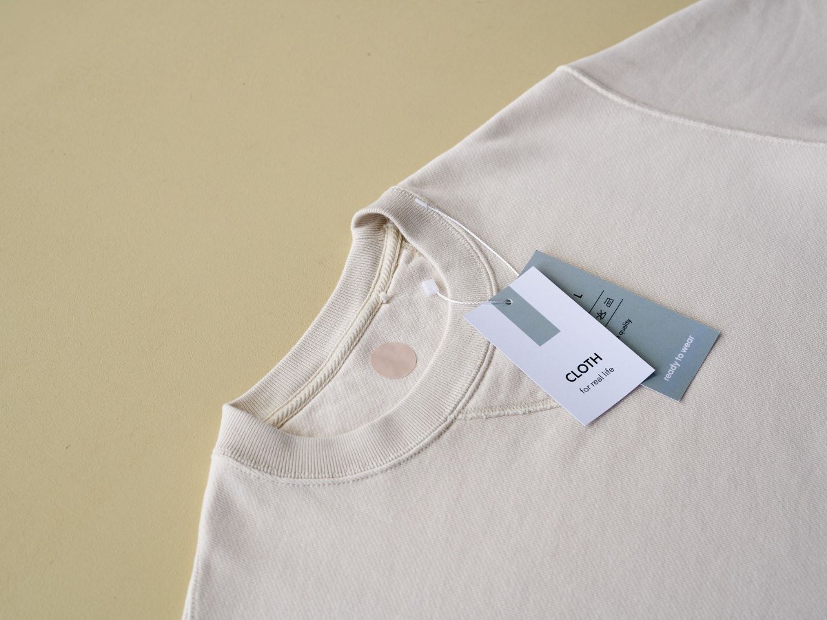 Un sweat-shirt beige avec ses etiquettes sur un fond jaune