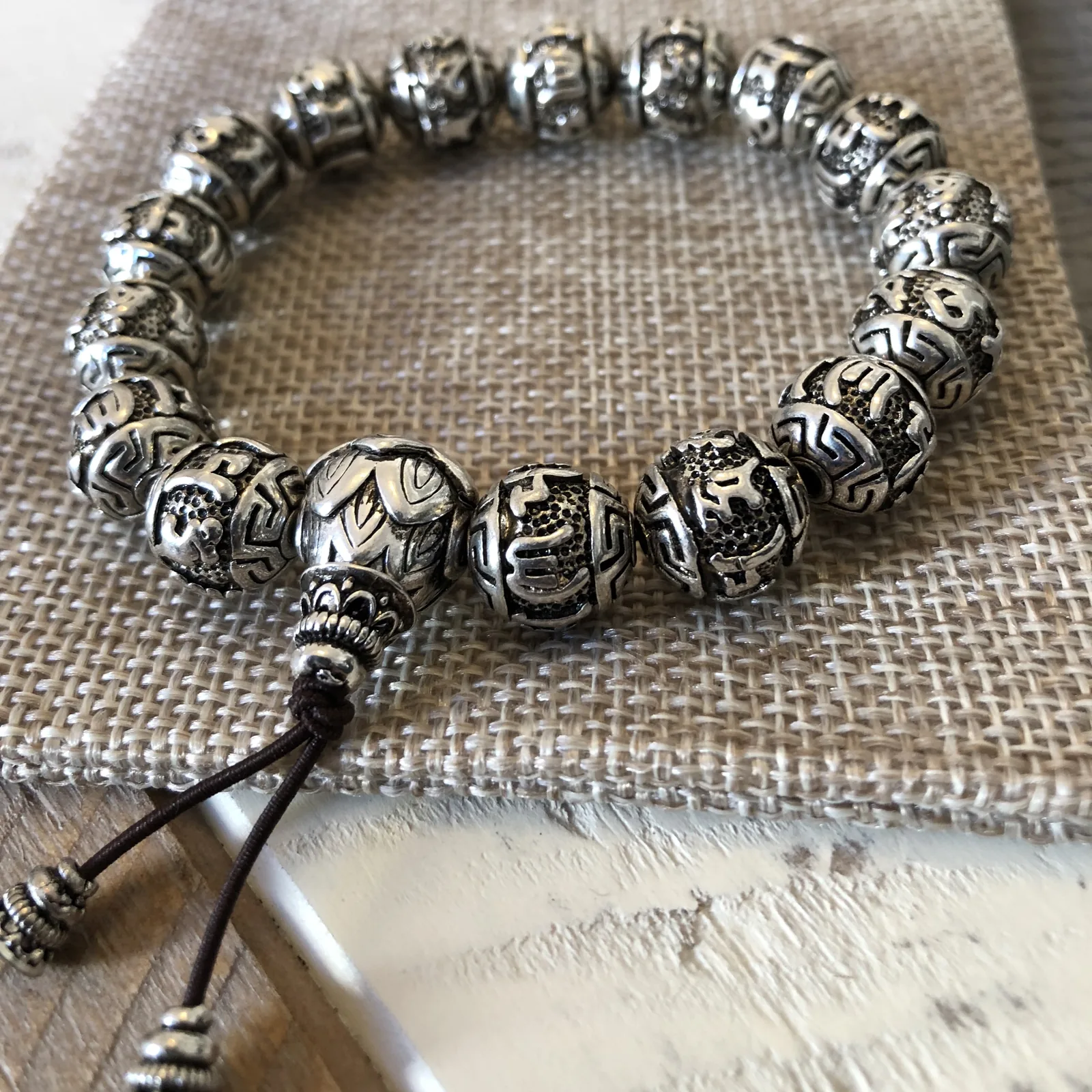 Bracelet de perles argentées gravées de motifs, fermé par un cordon coulissant