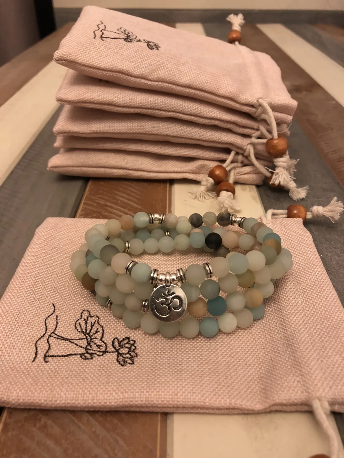 Mâlâ en amazonite mate posé sur une pile de pochettes en lin imprimées d’un lotus