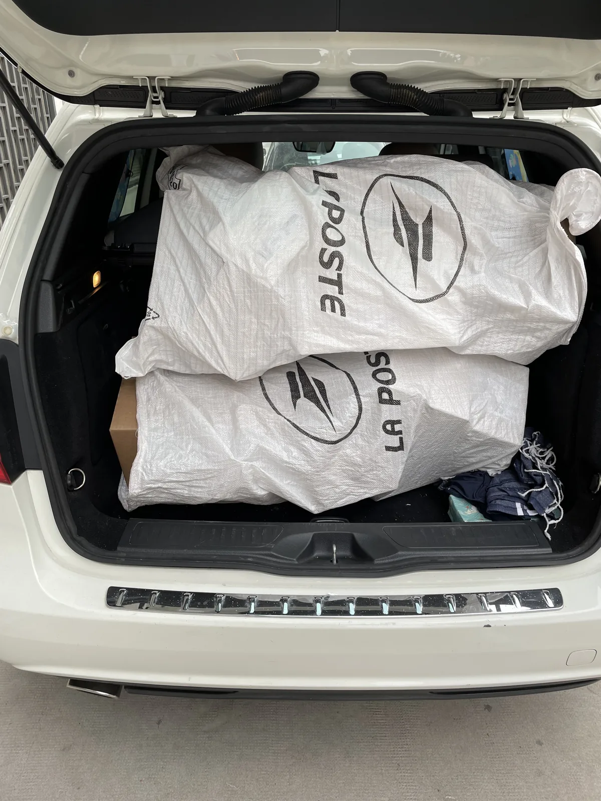 Deux sacs postaux remplis de colis chargés dans le coffre d’une voiture