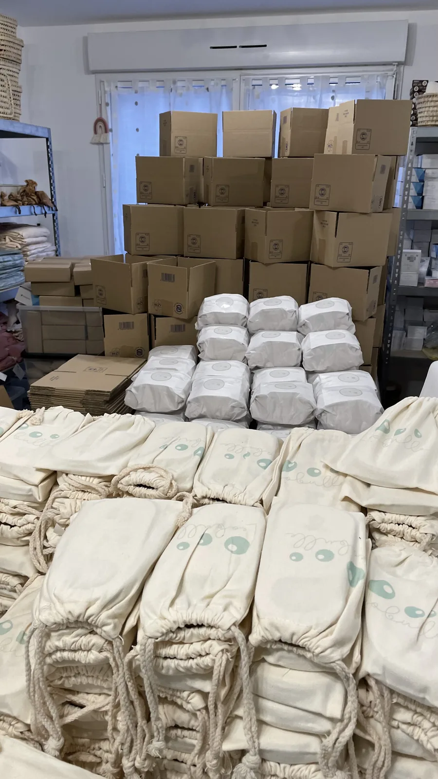 Pochons en coton imprimés au logo d’une marque, empilés devant un mur de cartons