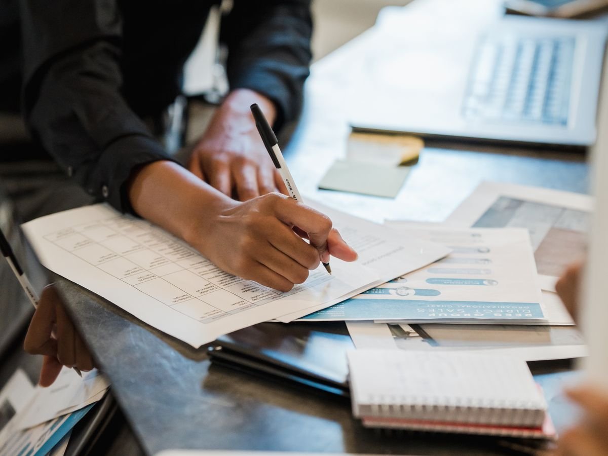 Des mains annotent au crayon des documents couverts de chiffres