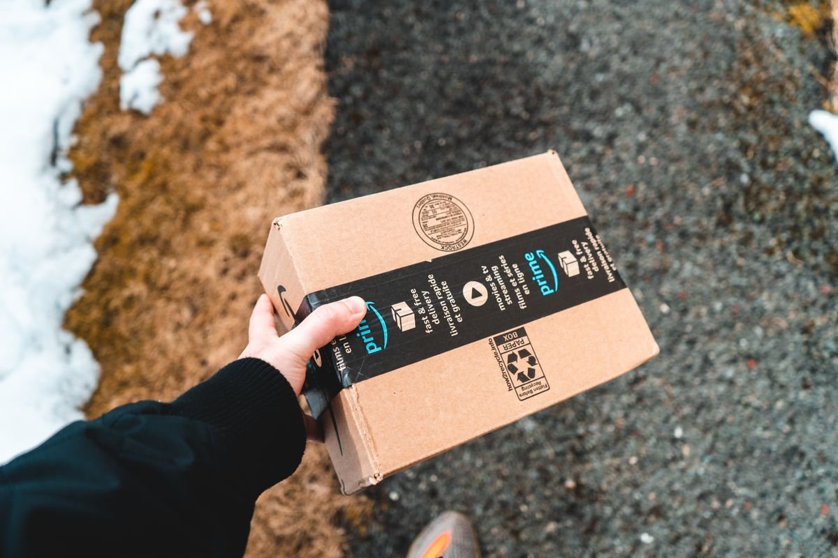 Une personne tenant un colis en carton Amazon Prime sur un trottoir urbain