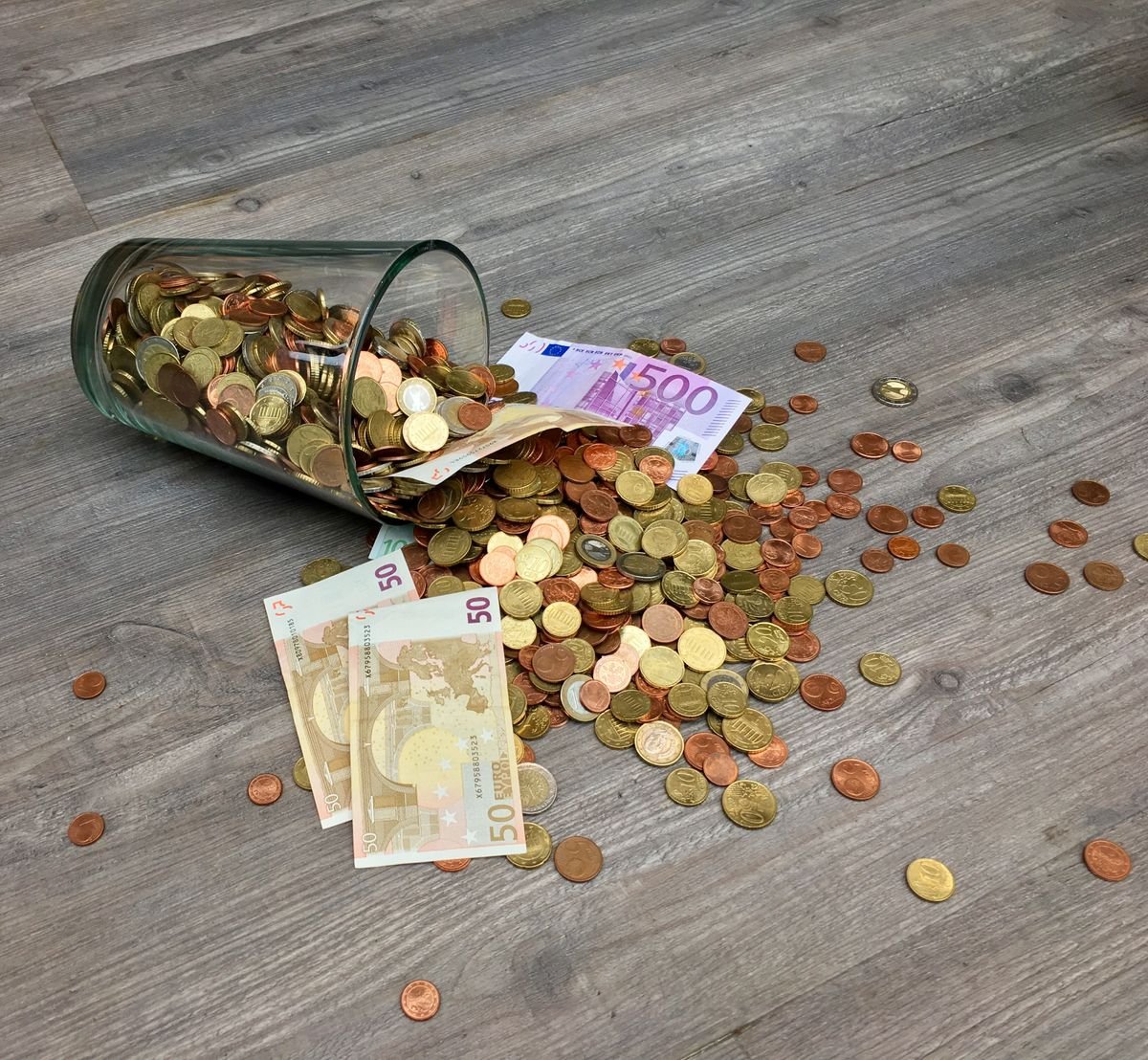 Un bocal en verre avec des pièces en euros et des billets renversés sur une