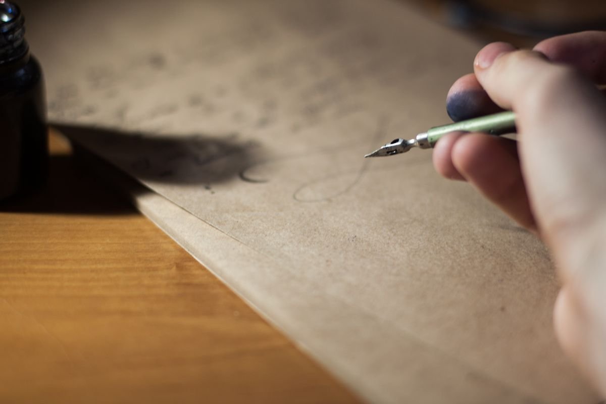 Gros plan d'une main écrivant avec un stylo plume sur du papier vintage