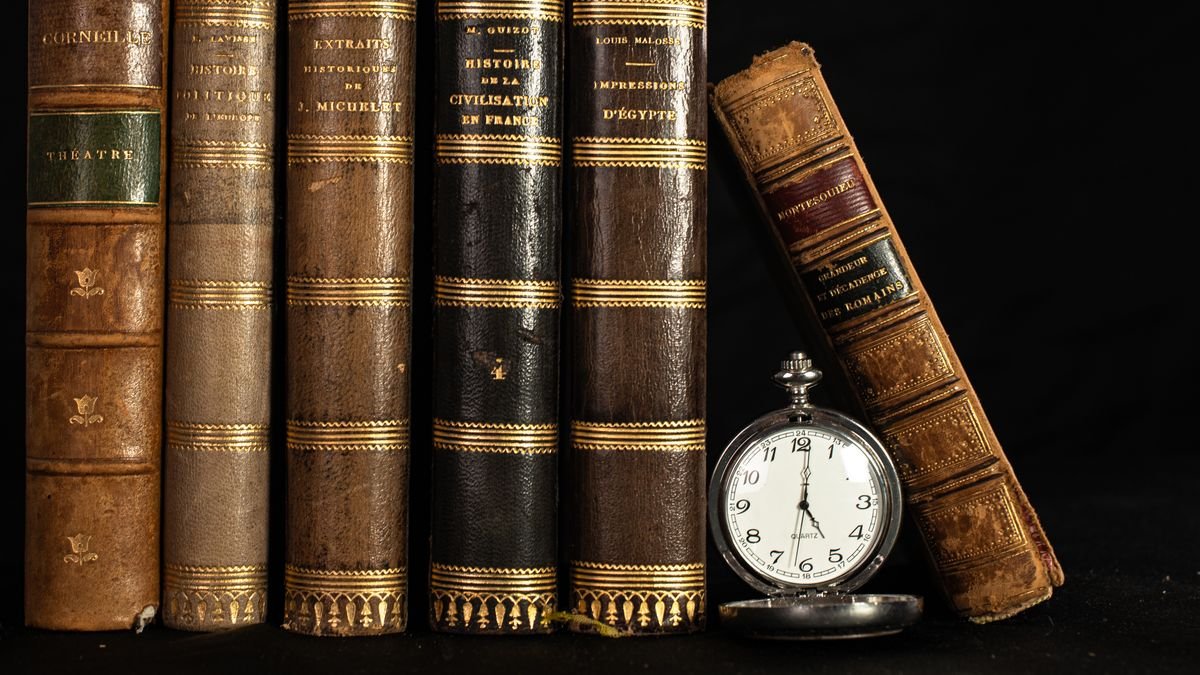 Une collection de livres anciens avec une montre de poche vintage sur fond noir