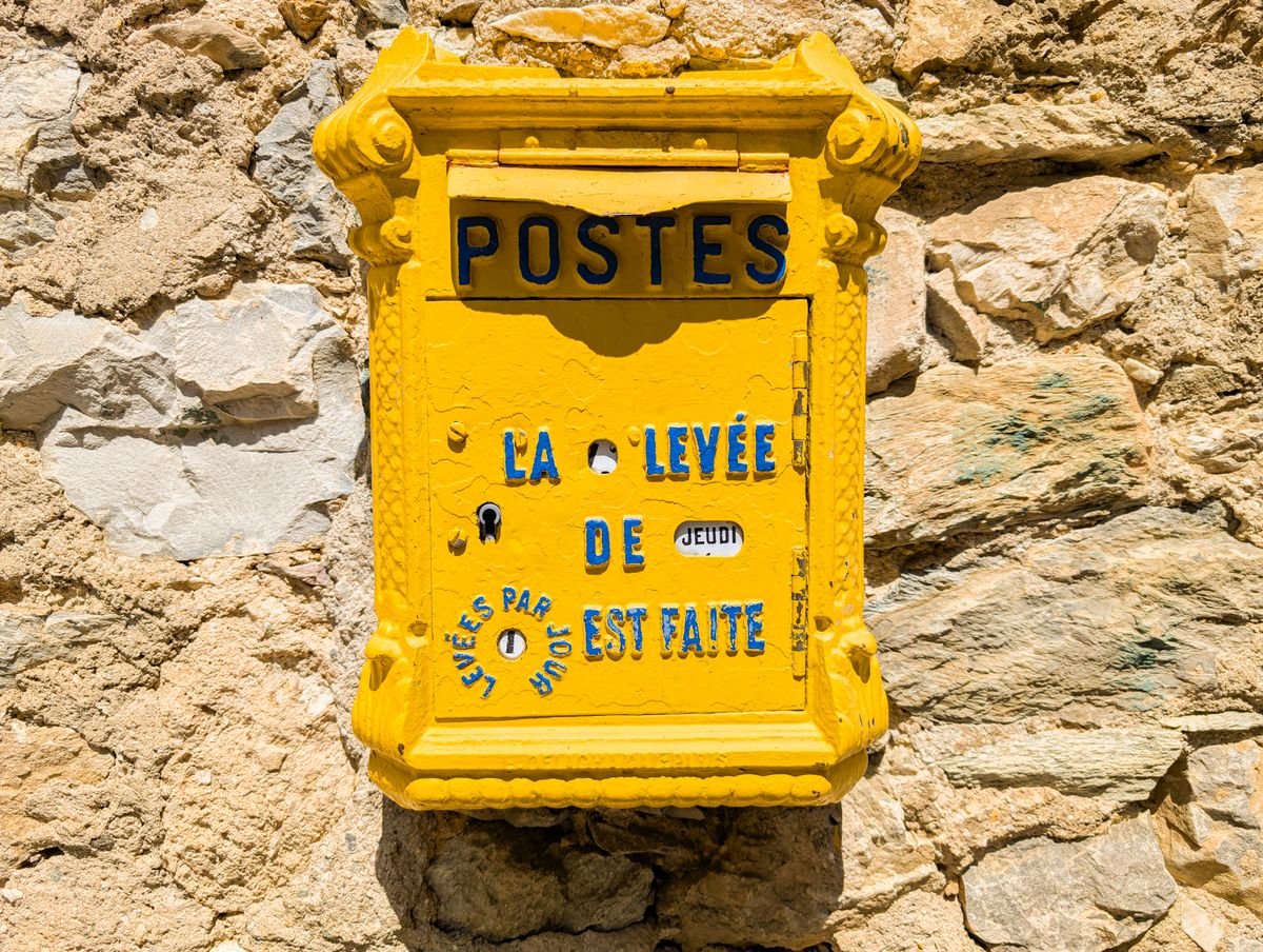 Boîte aux lettres française jaune classique sur un mur de pierre au soleil