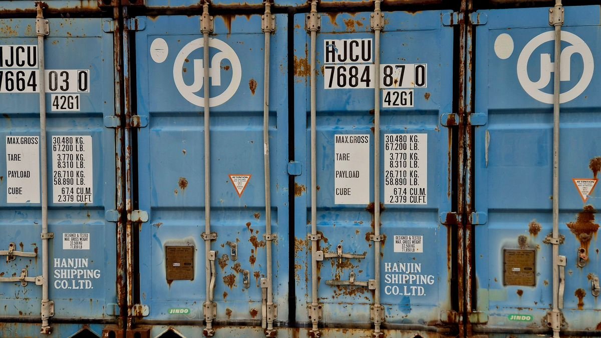 Le coût réel d’un colis : ce que personne ne compte Gros plan d'un conteneur d'expédition Hanjin bleu rouillé affichant des