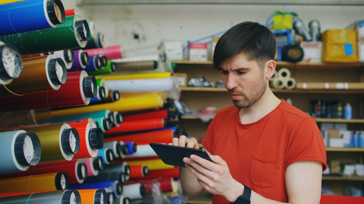 Un homme utilise une tablette numérique dans une imprimerie avec des rouleaux