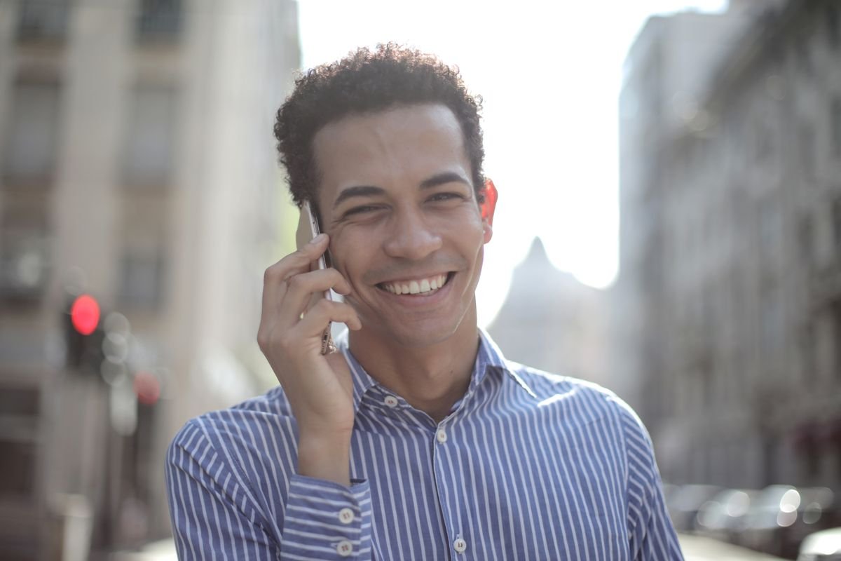 Jeune homme joyeux avec des cheveux bouclés profitant d'un appel téléphonique