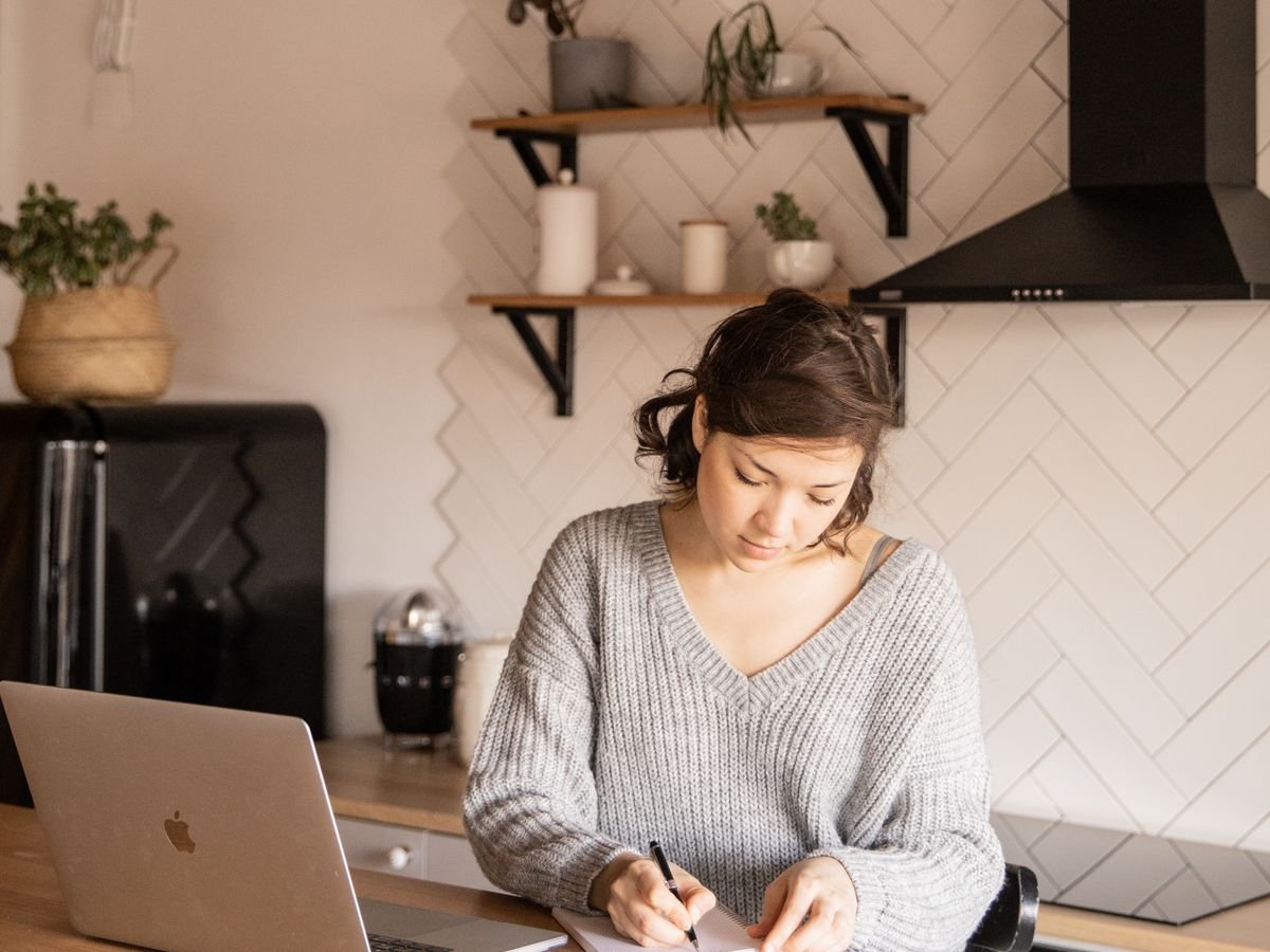 Une femme prend des notes devant un ordinateur portable, chez elle