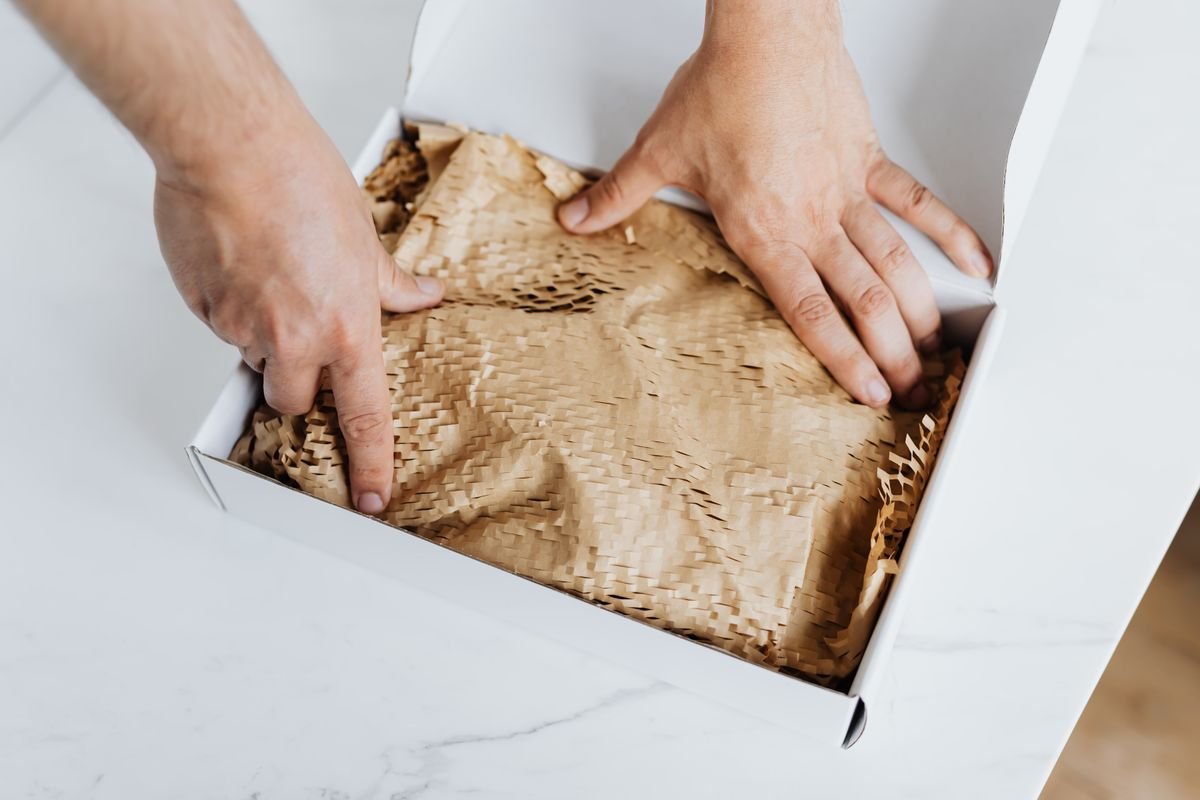 La nouvelle taxe sur les petits colis, expliquée simplement Gros plan sur des mains emballant une boîte en carton écologique avec du papier