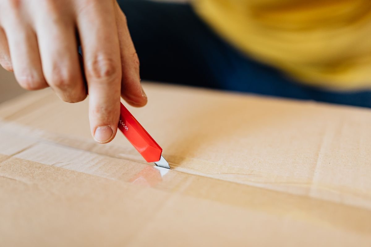 Le dropshipping vu de l’acheteur : le repérer, et vos droits Gros plan sur une personne utilisant un cutter rouge pour déballer un colis en