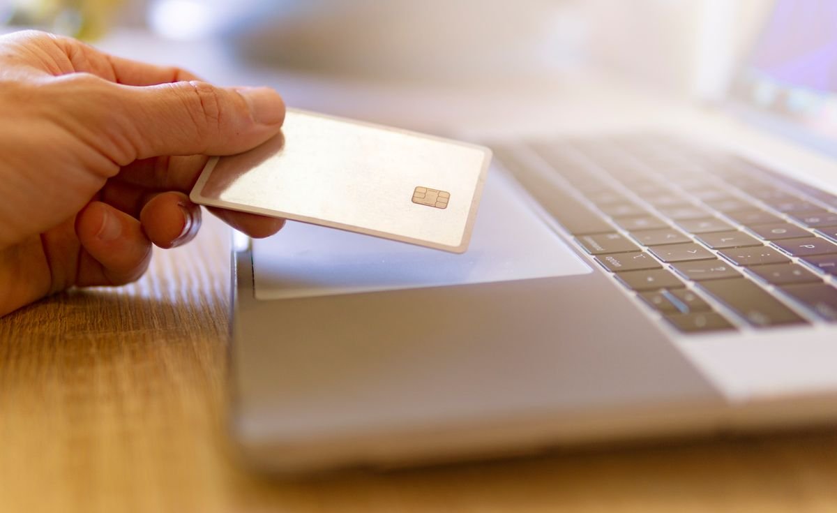Une personne tient une carte de crédit près d'un ordinateur portable pour des