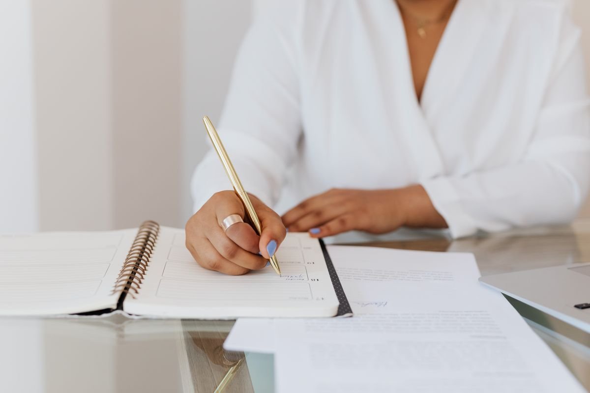 Gros plan sur une personne prenant des notes dans un agenda avec un stylo doré