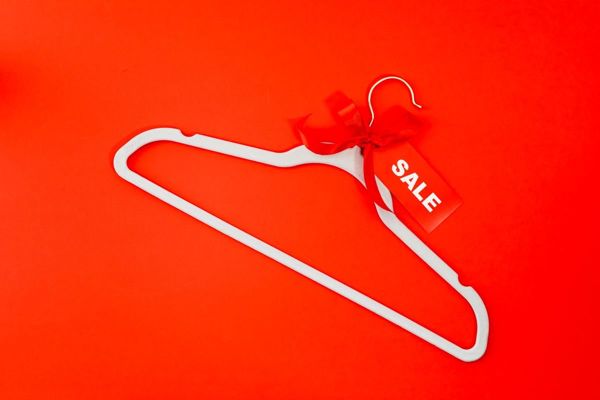 Un cintre blanc avec une étiquette de soldes rouge et un ruban sur un fond