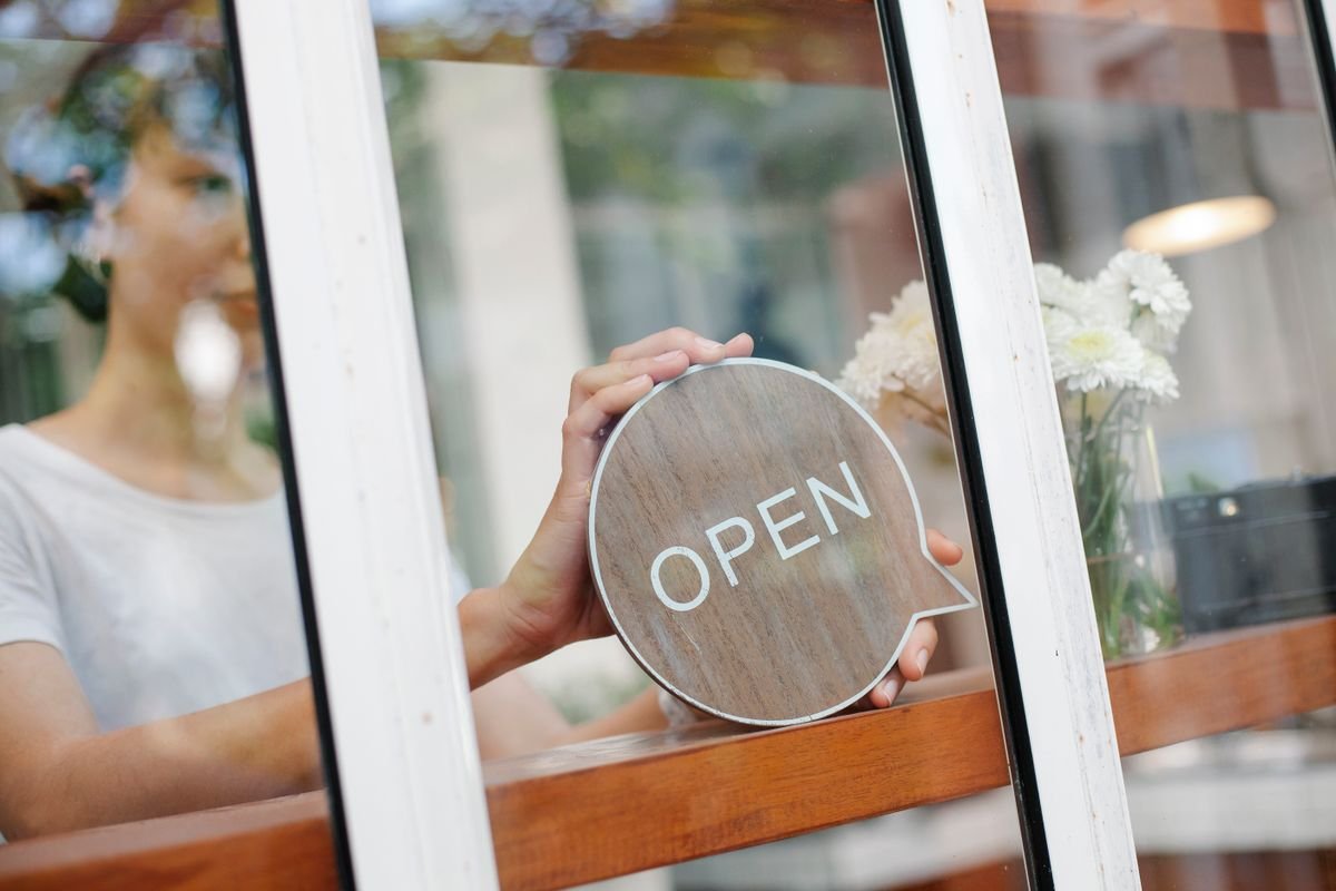 Une femme dans un café change le panneau pour 'ouvert'