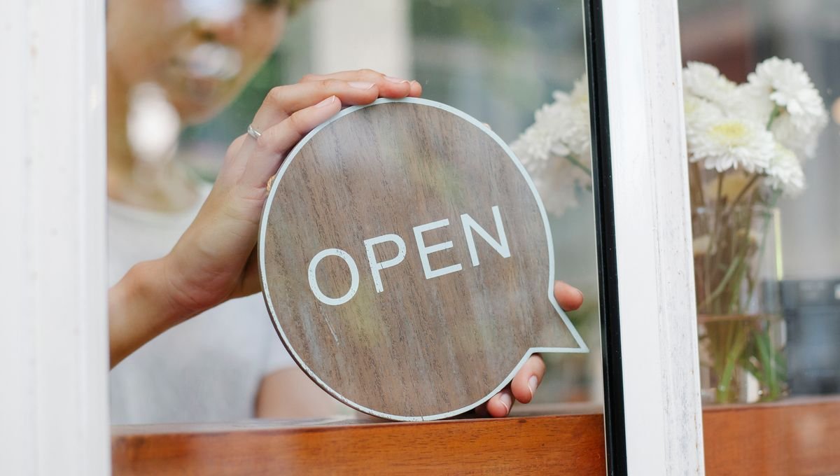 Une main place un panneau ouvert sur la porte d'un café avec des fleurs