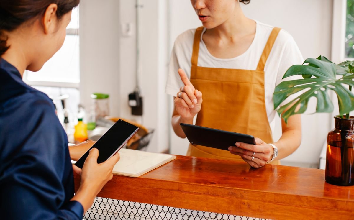 Choisir sa plateforme e-commerce : la méthode, pas le classement Deux femmes interagissant avec des appareils numériques au comptoir d'un café