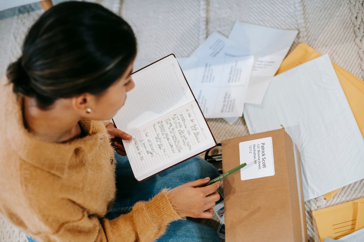 Une jeune femme assise par terre en organisant son courrier et ses colis