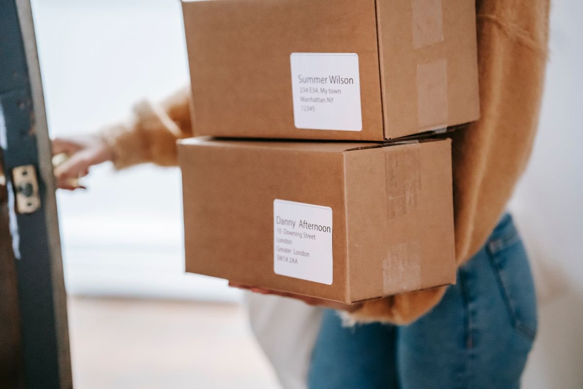 Le coût réel d’un colis : ce que personne ne compte Une femme livrant deux cartons en carton dans un appartement intérieur