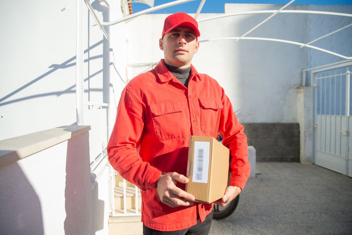 Un livreur masculin en uniforme rouge tenant un colis à l'extérieur au Portugal