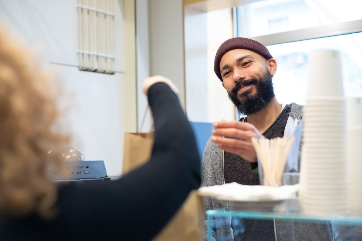 Un barista souriant remet un sac en papier à un client dans un café accueillant