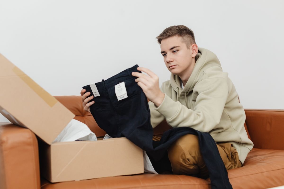 Récolter des avis clients : la méthode qui m'en a apporté 2 189 Adolescent assis sur le canapé déballant des vêtements neufs d'une boîte en
