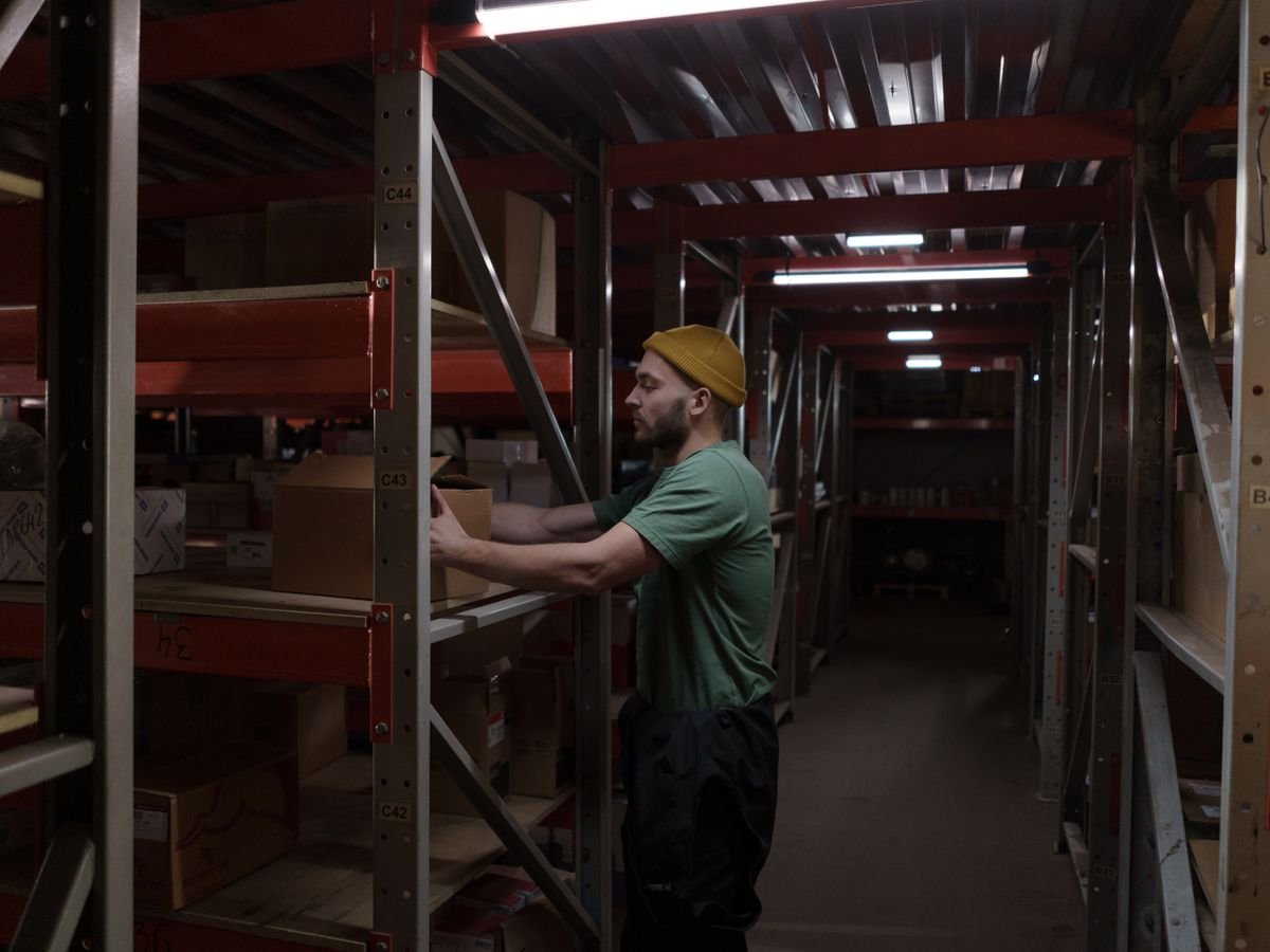 Vendre sur Amazon : les deux choix à faire, et ce qu’ils coûtent Un homme range des cartons sur les rayonnages d’un entrepôt