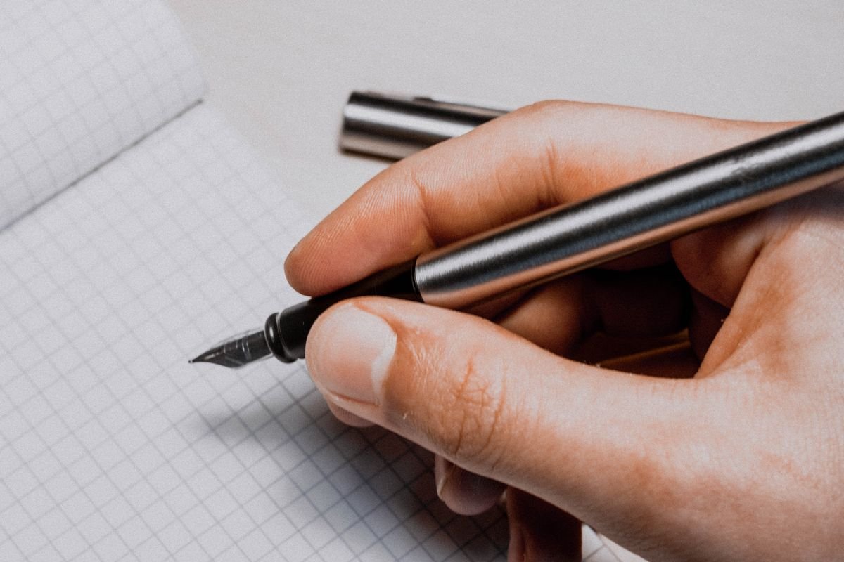 Un gros plan détaillé d'une main tenant un stylo plume au-dessus d'un papier