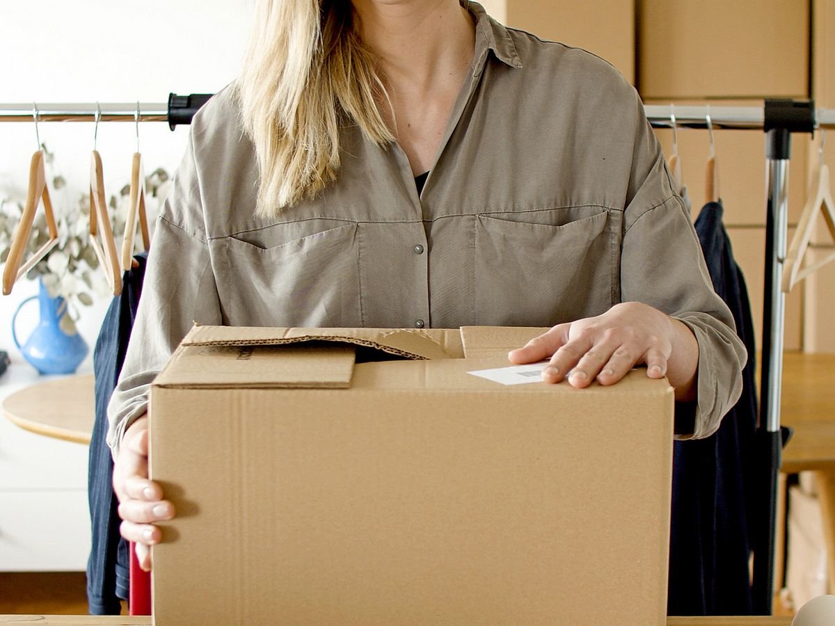 Une femme porte un carton devant un portant de vêtements