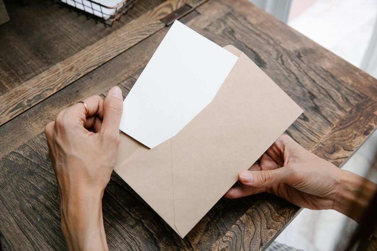 Des mains tenant une lettre à l'intérieur d'une enveloppe marron sur un bureau