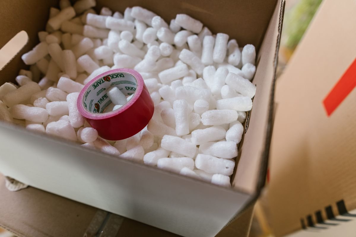 Frais de port : le paramétrage qui protège votre marge Gros plan sur une boîte en carton remplie de billes de polystyrène et de ruban