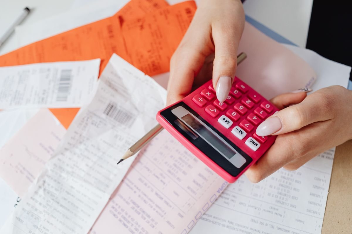 Le coût réel d’un colis : ce que personne ne compte Mains utilisant une calculatrice rose pour gérer des dépenses parmi divers