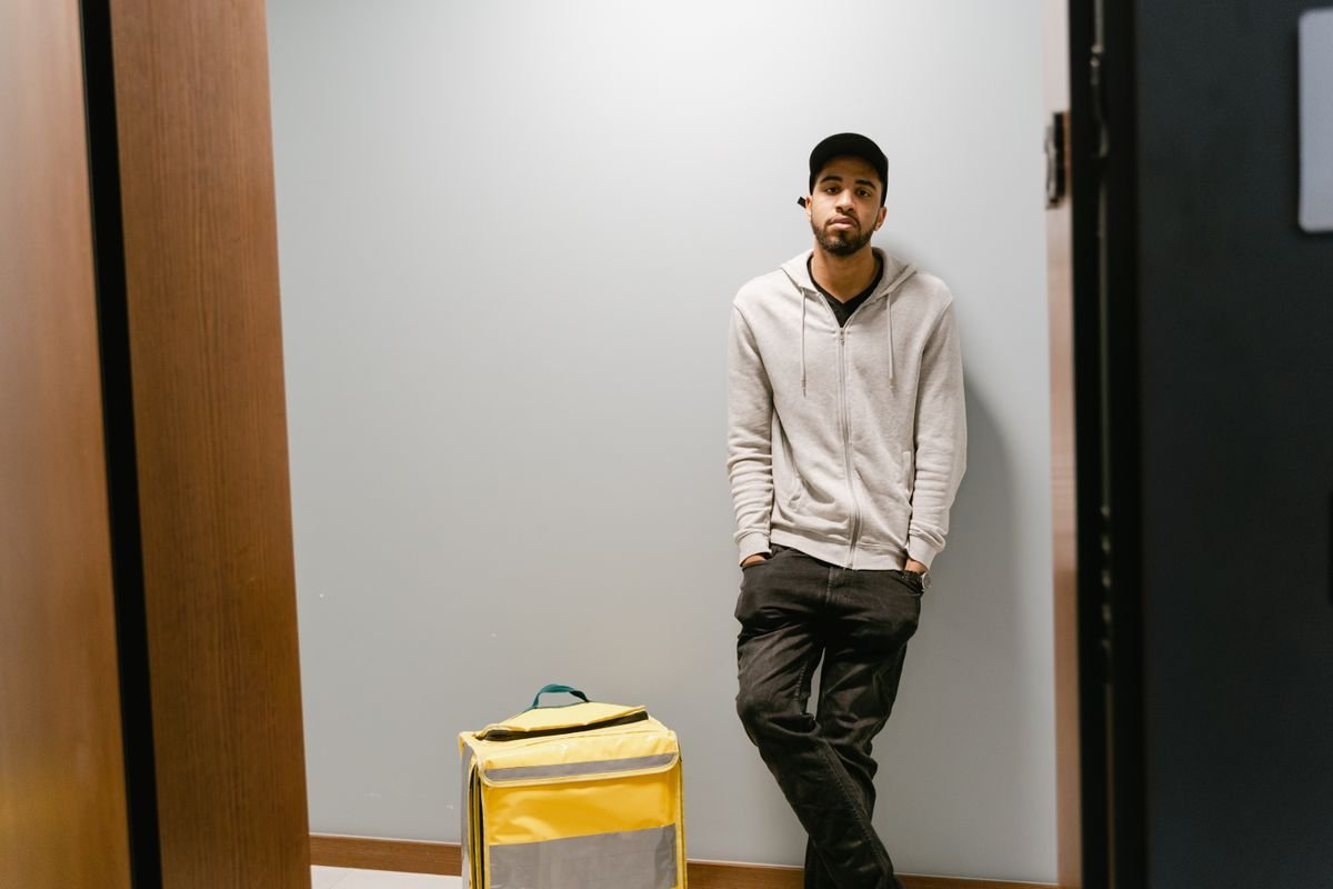 Jeune homme livreur attendant à l'intérieur avec un sac thermique jaune, prêt