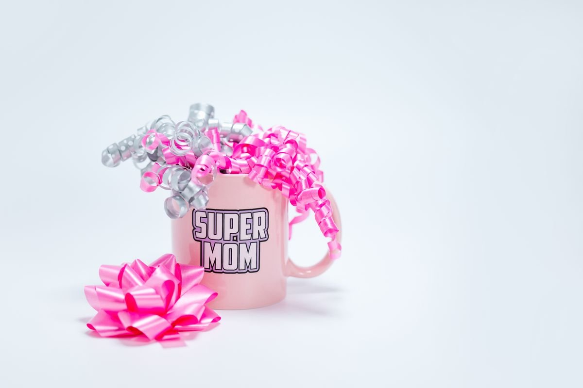 Un mug Super Maman rose orné de rubans roses et argentés sur fond blanc