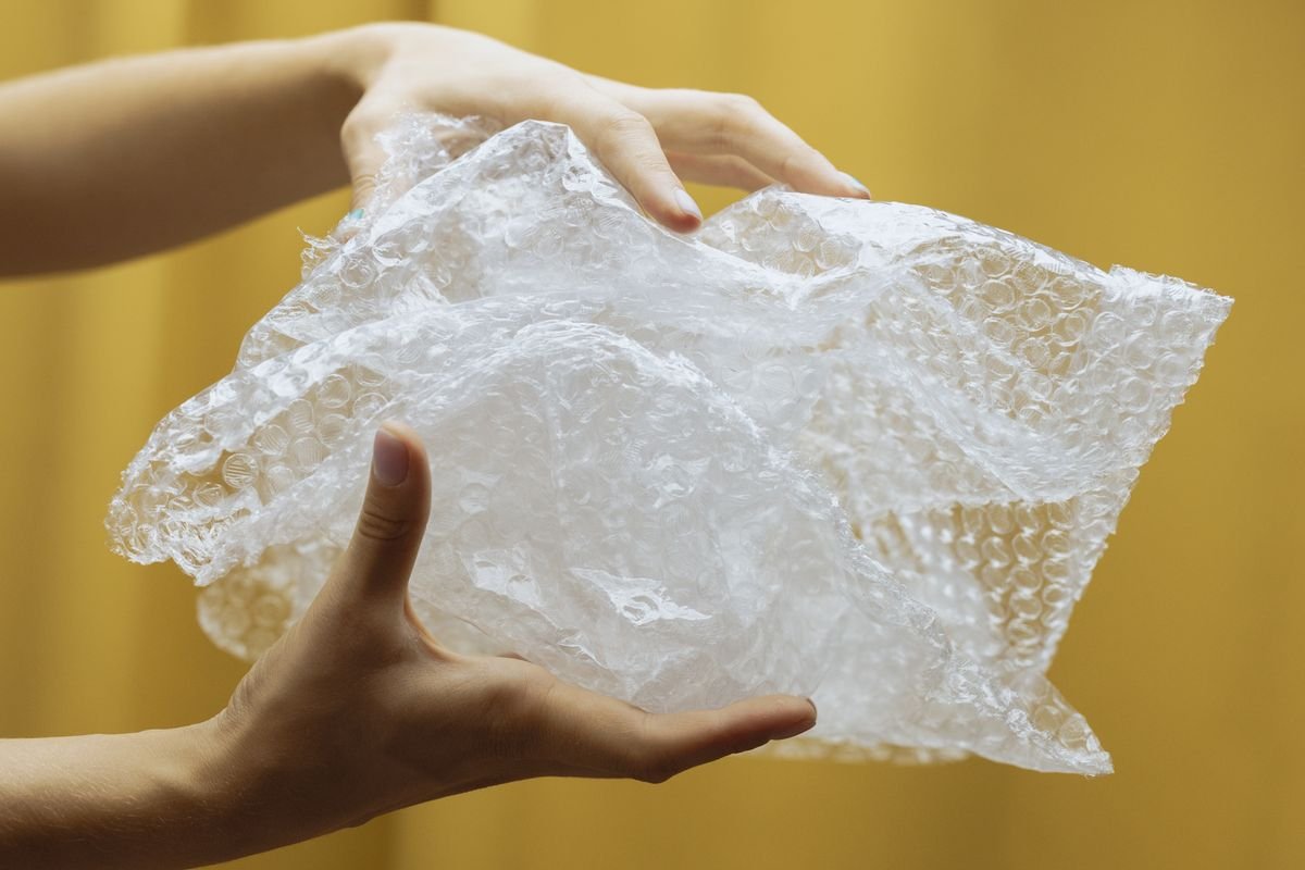 Le coût réel d’un colis : ce que personne ne compte Gros plan sur des mains tenant et froissant du papier bulle sur un fond jaune à