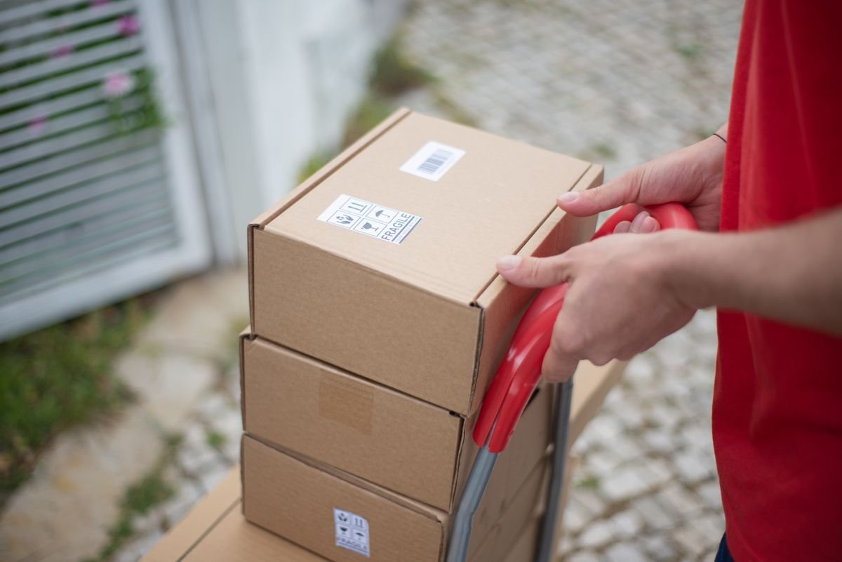 La nouvelle taxe sur les petits colis, expliquée simplement Gros plan de mains tenant un chariot avec des cartons empilés à l'extérieur