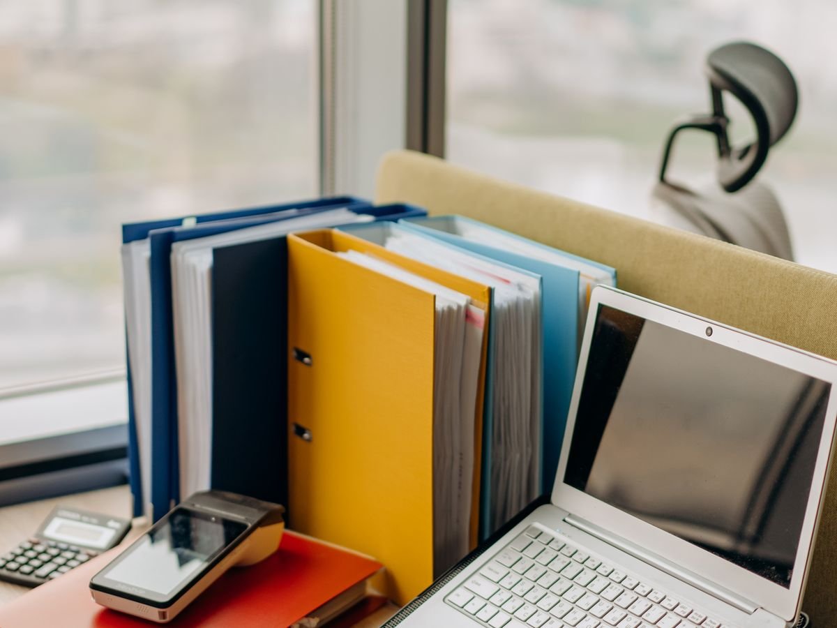 Des classeurs colorés empilés à côté d’un ordinateur portable