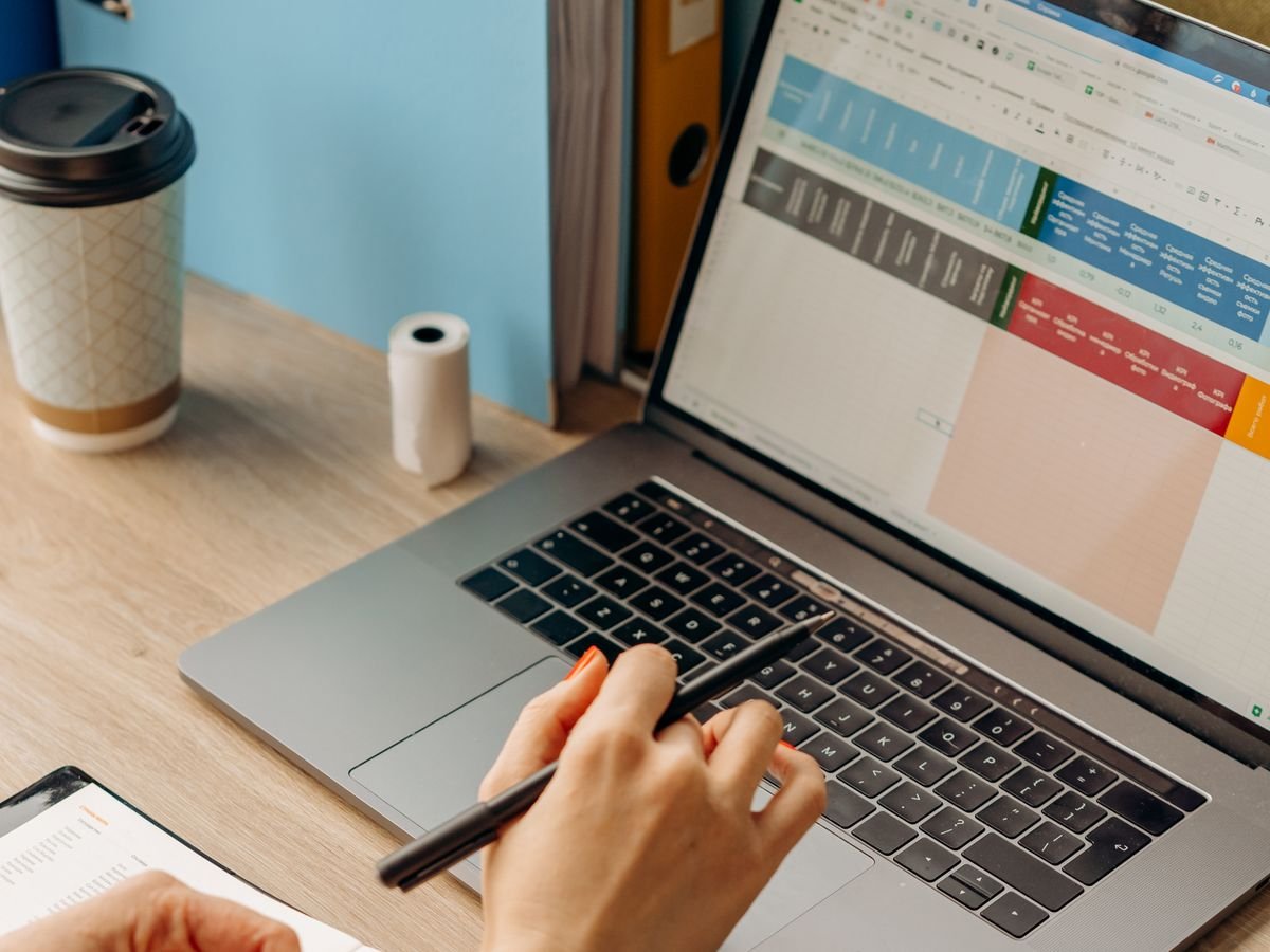 Une main écrit à côté d’un ordinateur portable ouvert
