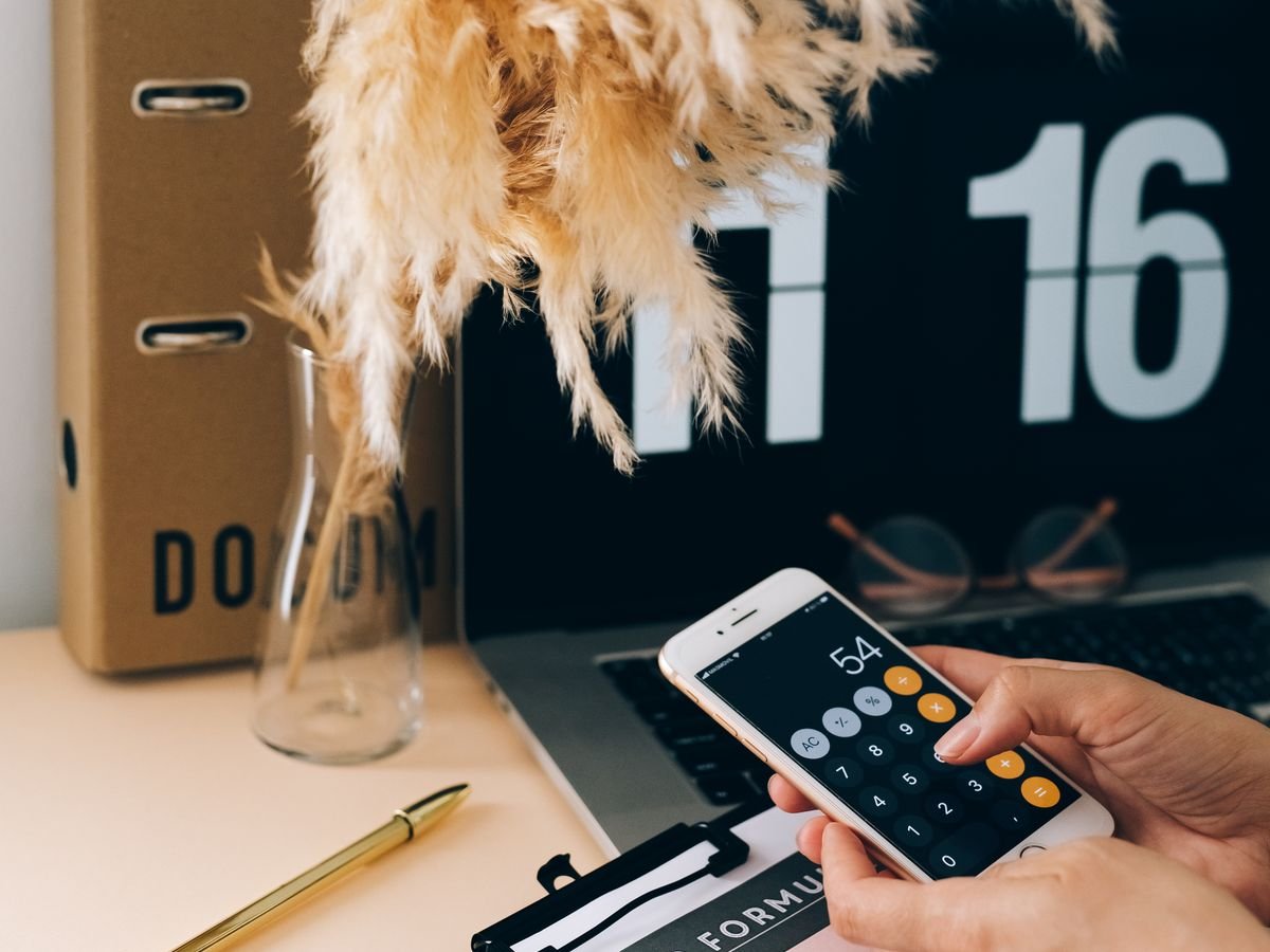 Le calcul de marge en e-commerce : de la vente à ce qui reste Une main tape sur la calculatrice d’un téléphone, entourée de cartons