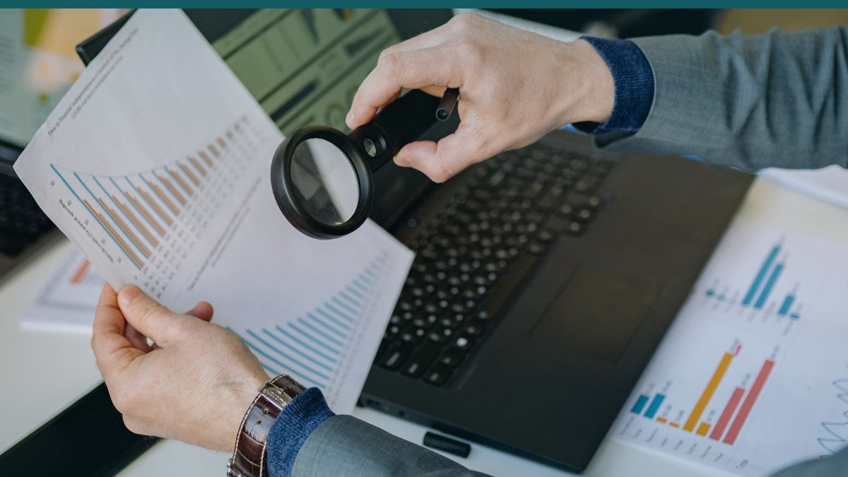 Une personne examine un document a la loupe devant un ordinateur portable
